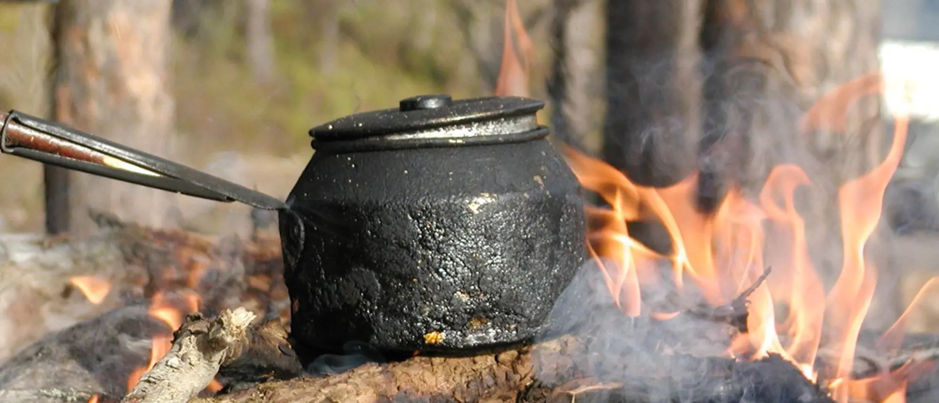 Eld brinner i en eldstad utomhus. En kaffepanna står på elden.