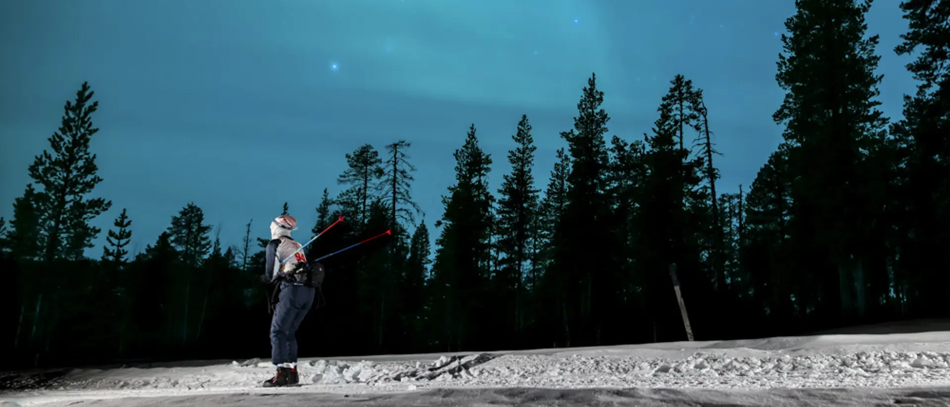 Foto av en man som åker längdskidor under norrsken