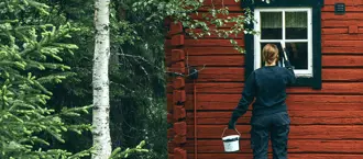 En kvinna målar om en stuga i skogen. Foto.