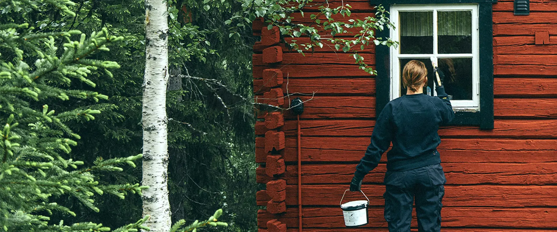 En kvinna målar om en stuga i skogen. Foto.