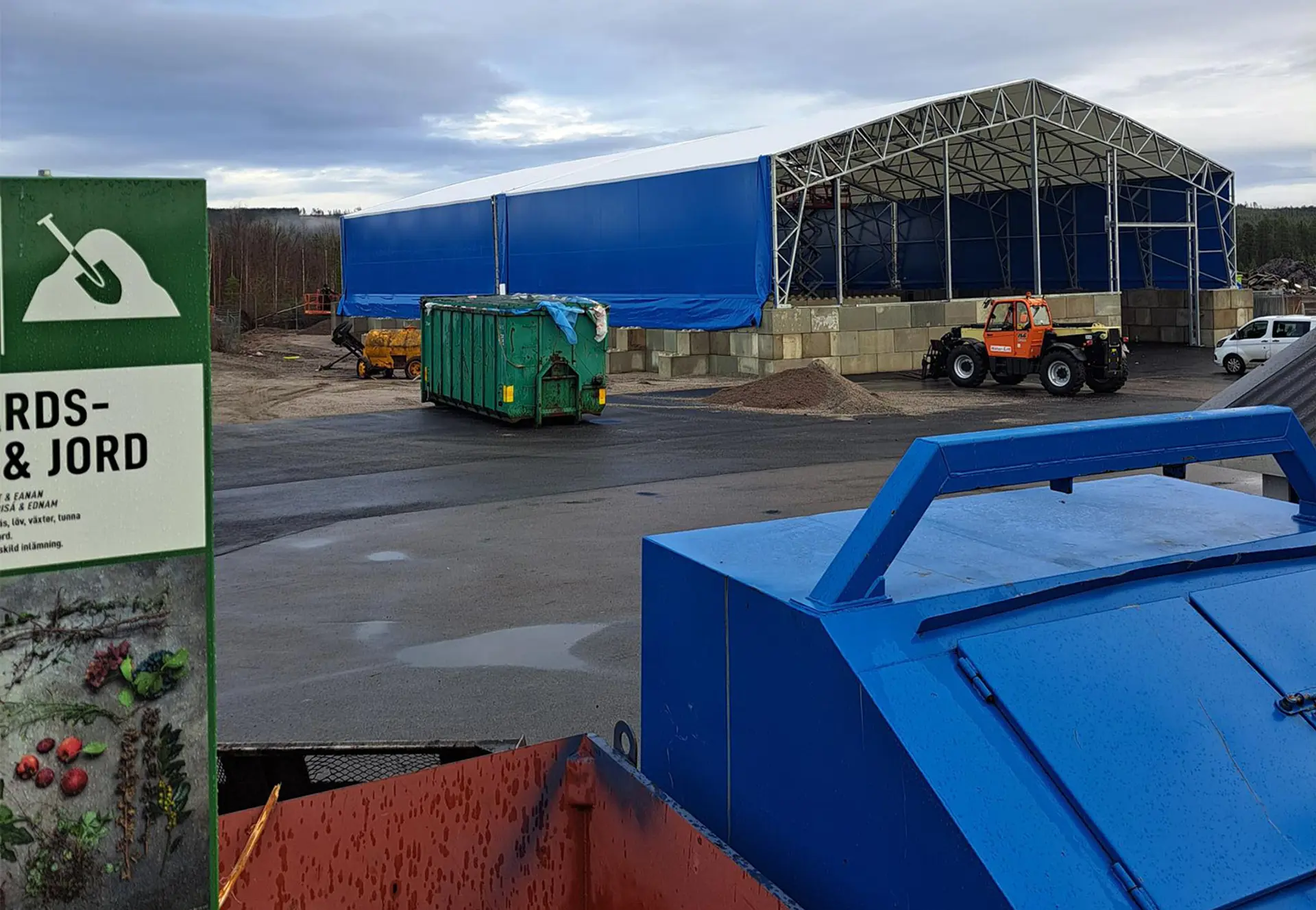 Bild av omlastningsstationen nere på återvinningscentralens område. Den består av betongsarg, en stålkonstruktion och en blå tältduk. Foto.