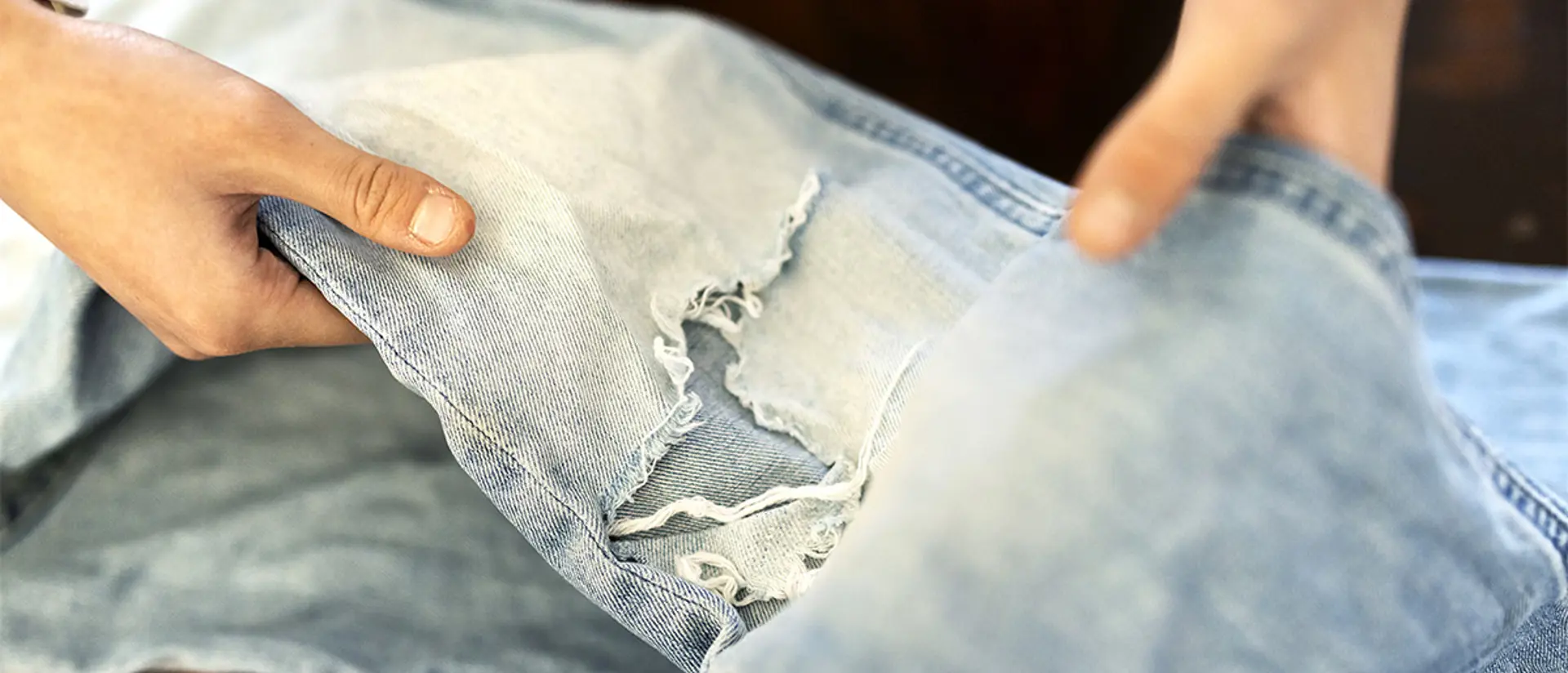Person som håller upp trasiga jeans. Foto.